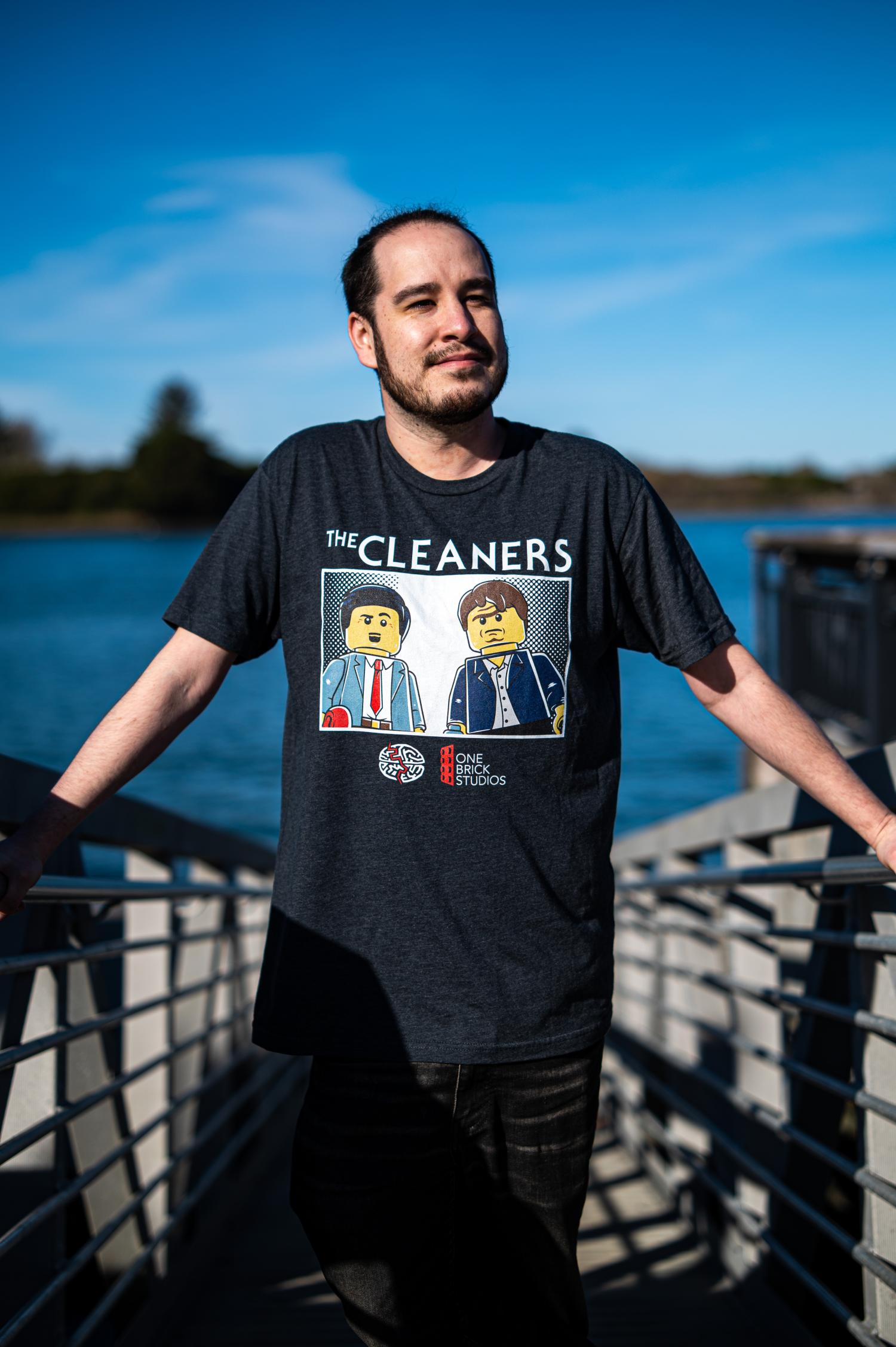 Zach Macias standing on a dock wearing a grey shirt with a logo for a LEGO stop motion film called "The Cleaners." Under that are logos for MindGame Studios and One Brick Studios.